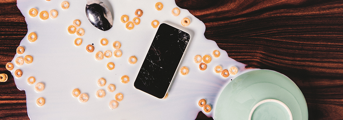 Utspilld mjölk och flingor på ett bord. En trasig mobiltelefon som ersätts genom hemförsäkring ligger på bordet.